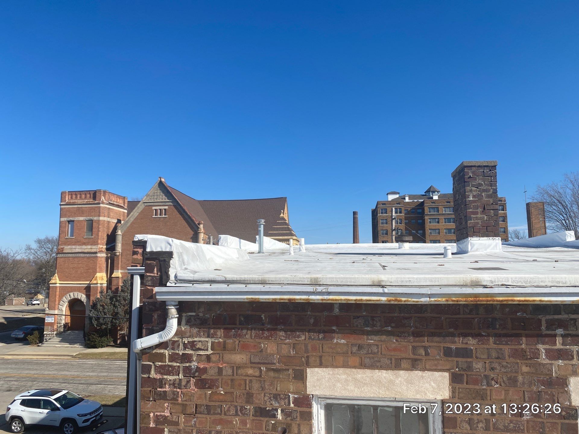 Snow-covered rooftops and brick buildings under a clear blue sky, with a parked car below.