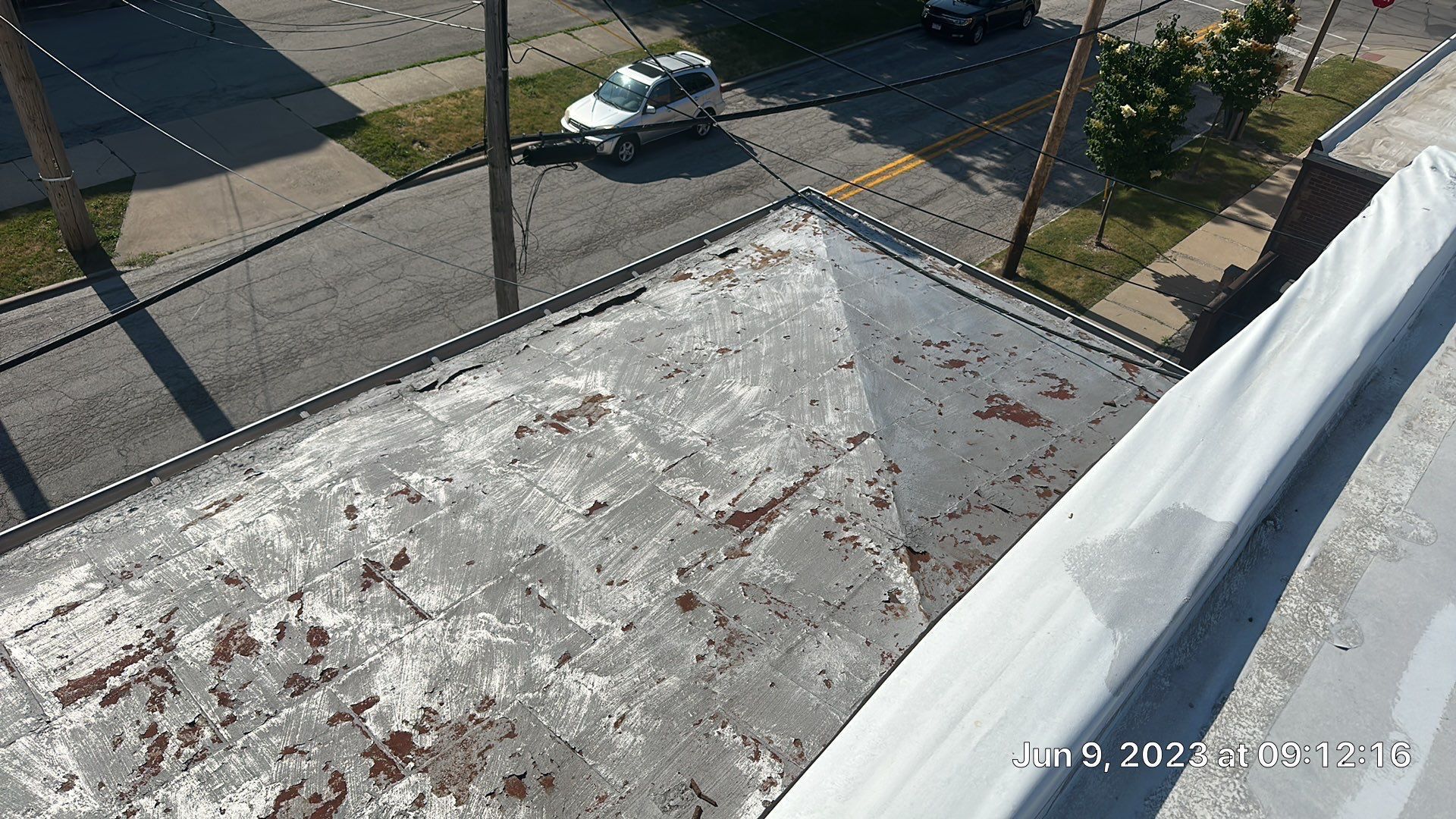 Rooftop with weathered flat surface beside a white roof edge, overlooking a street with parked cars below.