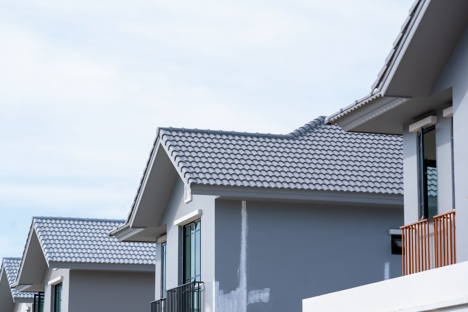 Row of modern houses with gray tiled roofs against a bright sky