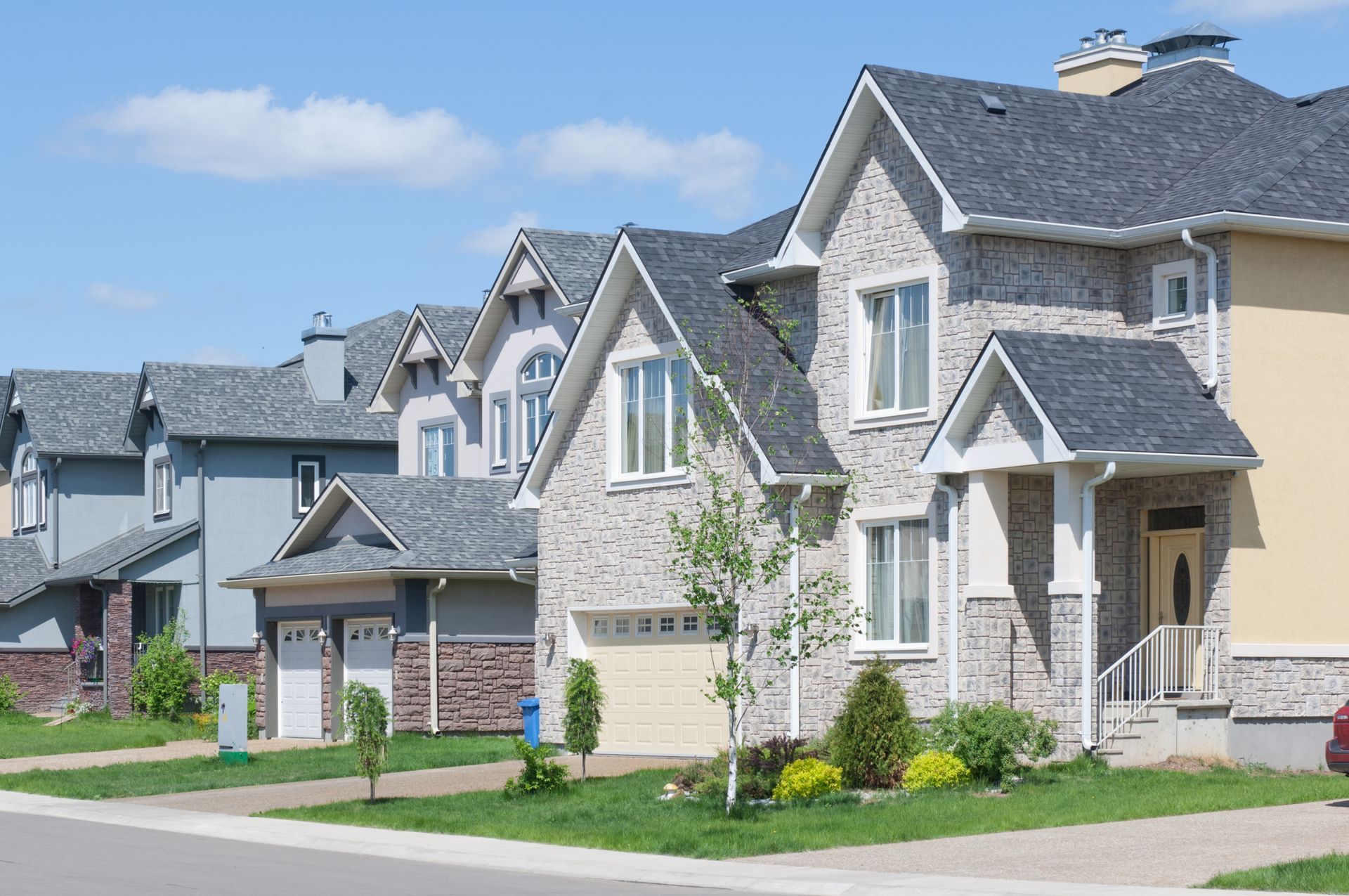 Suburban row of modern stone houses with gabled roofs and green lawns on a sunny day