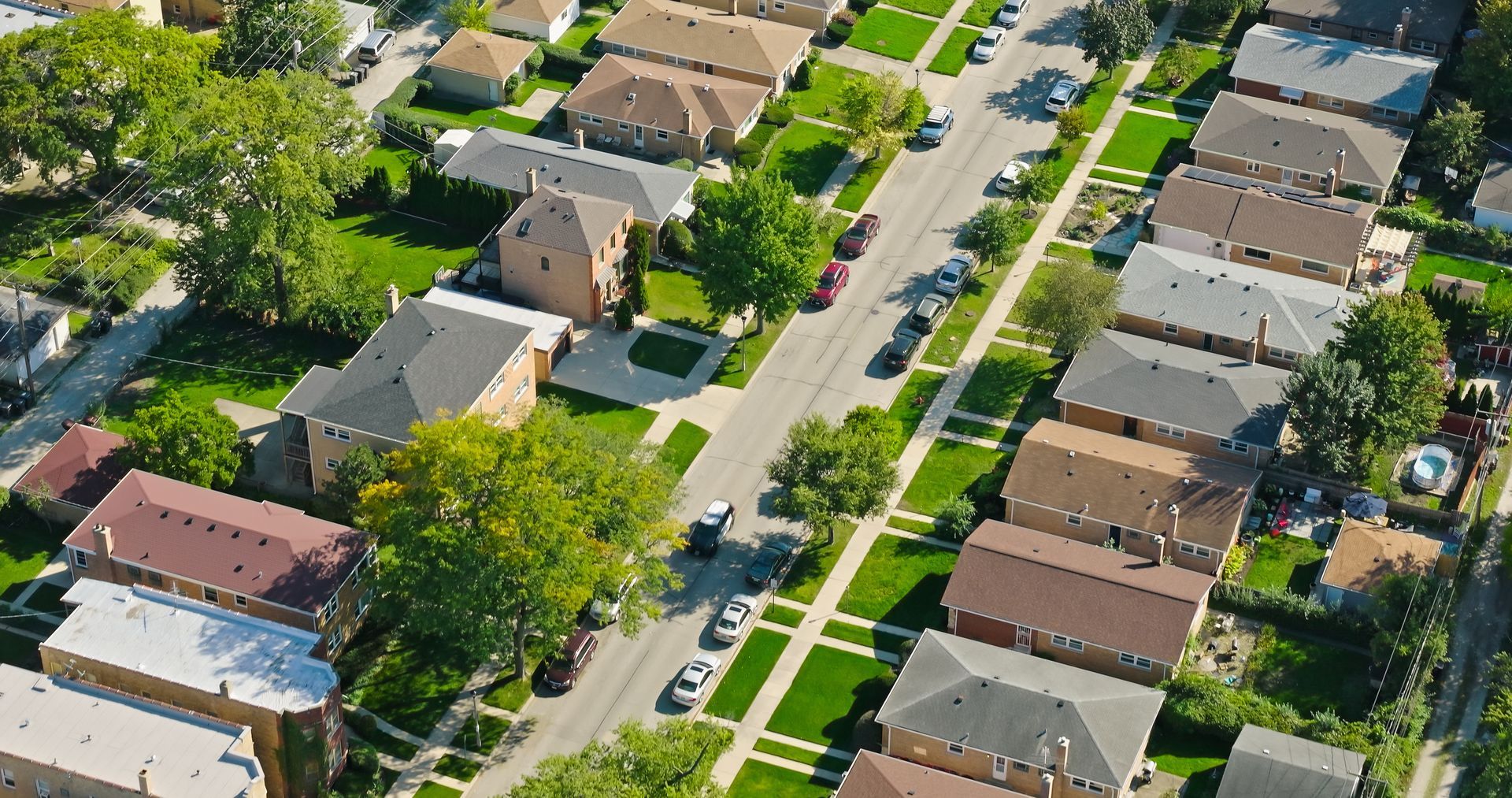 Aerial view of a suburban neighborhood with houses, trees, and a tree-lined street.