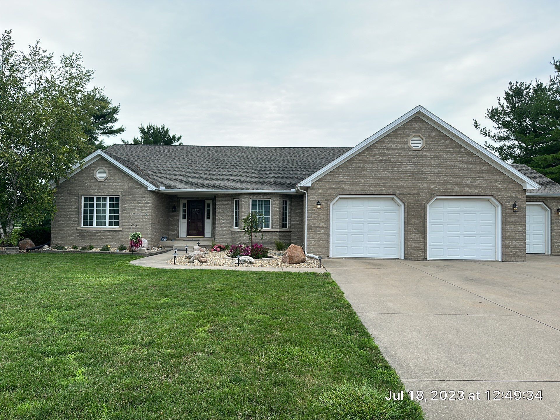 Single-story brick house with two white garage doors, front lawn, and landscaped flower bed