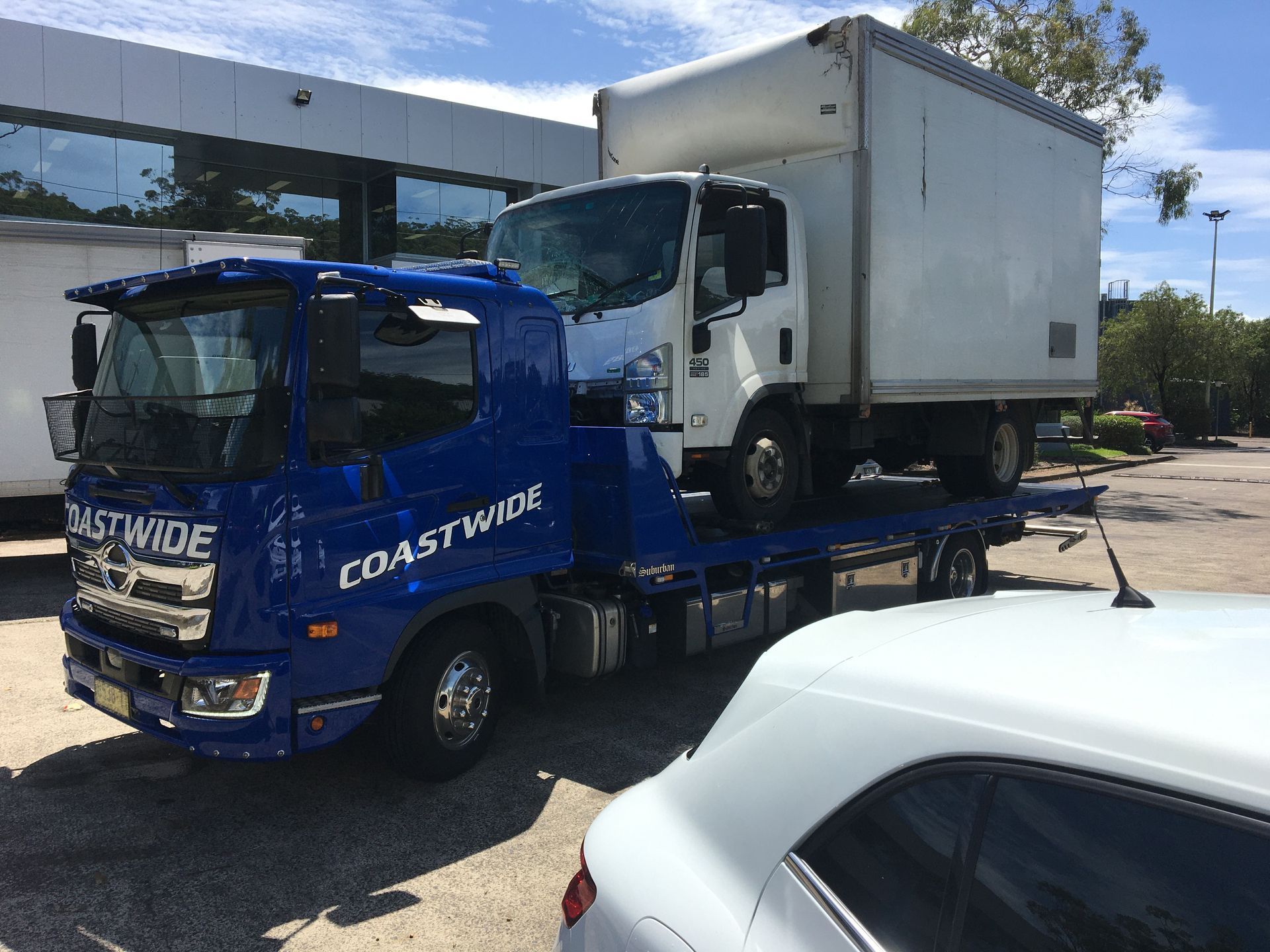 Blue Coastwide tow truck carrying a white box truck on a sunny day. — Coastwide Towing & Transport In Berkeley Vale, NSW