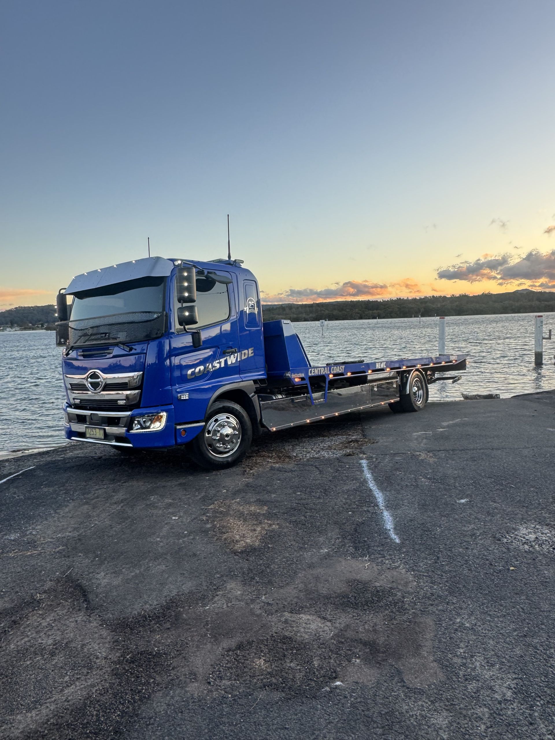 Blue tow truck parked on a pier, with water and sunset in the background. — Coastwide Towing & Transport In Berkeley Vale, NSW