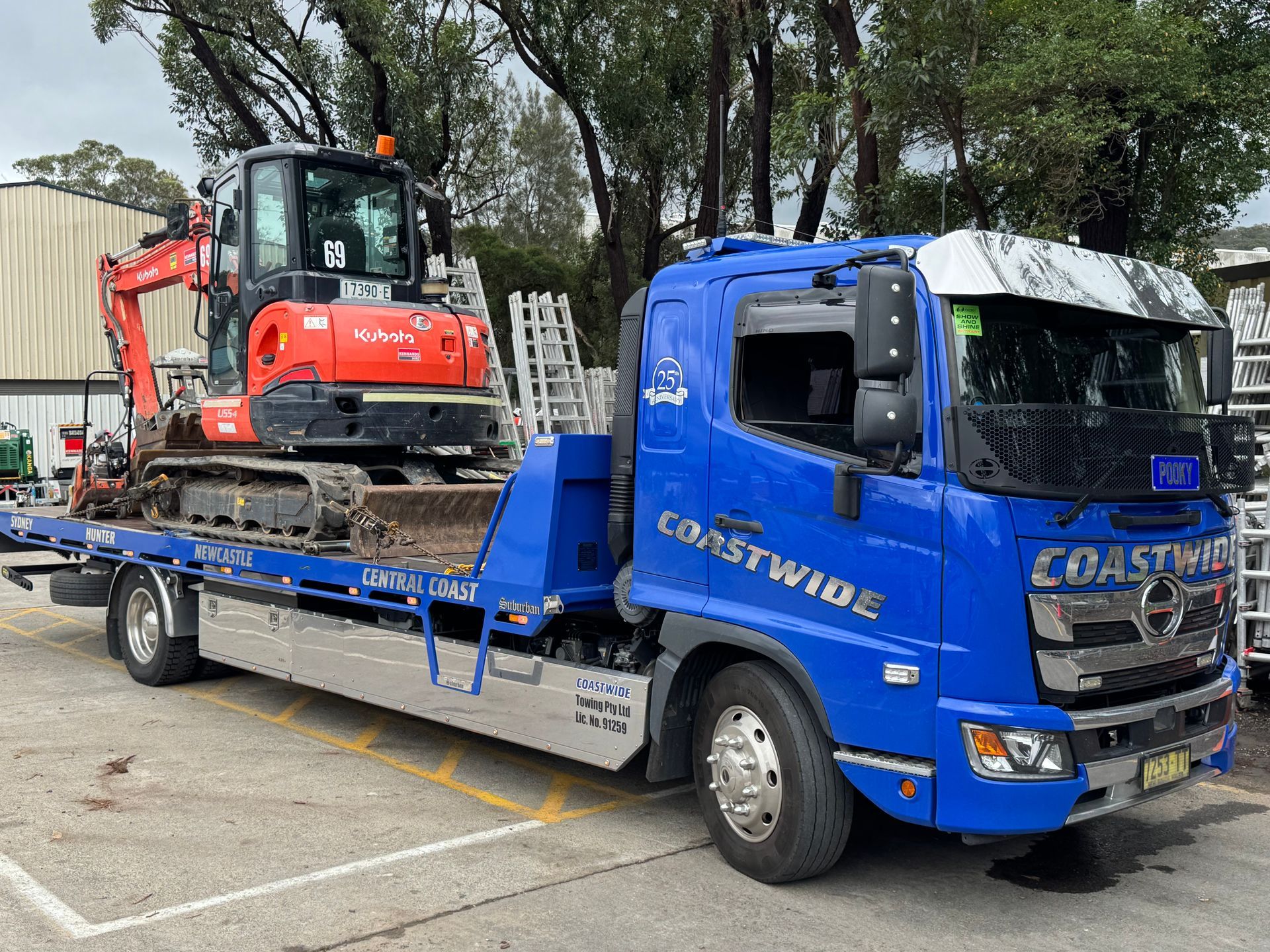 Blue Coastwide truck carrying an orange excavator on a flatbed, parked in a lot. — Coastwide Towing & Transport In Berkeley Vale, NSW