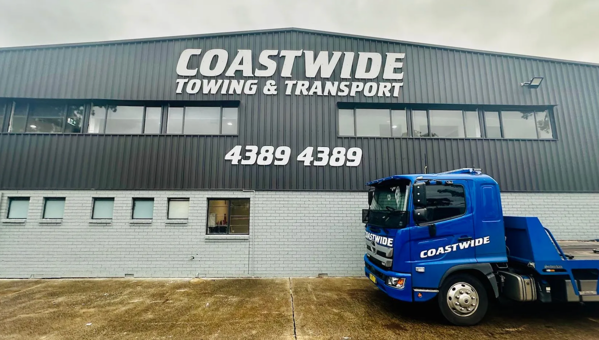 A blue pick-up truck parked in front of the Coastwide Towing & Transport warehouse.