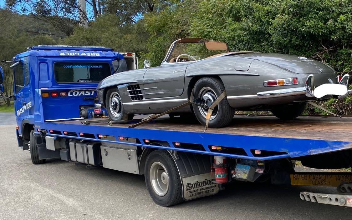 Tilt Tray Truck Transporting A Classic Grey Convertible Sports Car Safely On A Flatbed Tow Truck
