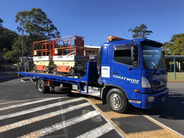 A blue tow truck with coastwide written on the side is carrying heavy equipment — Coastwide Towing & Transport In Berkeley Vale, NSW