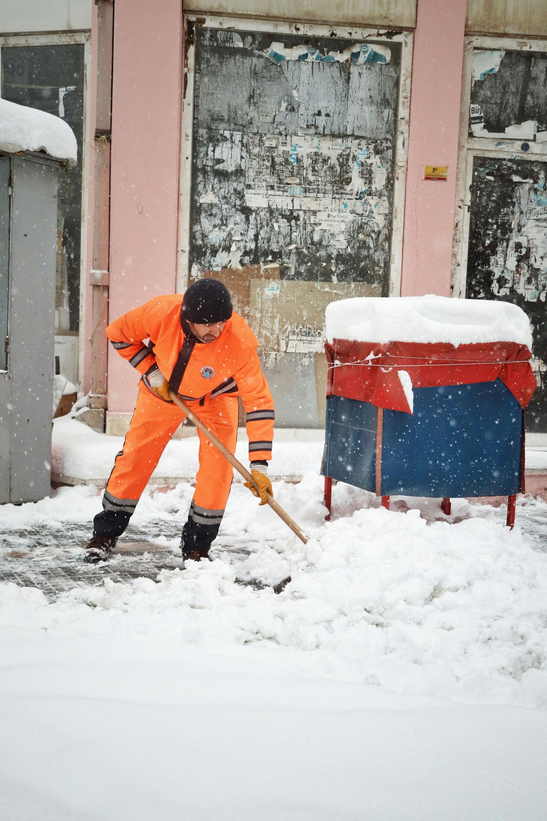 Person in orange snowsuit shoveling snow in front of a building.