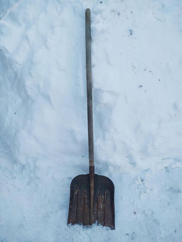 A rusty shovel with a wooden handle lying on snow.