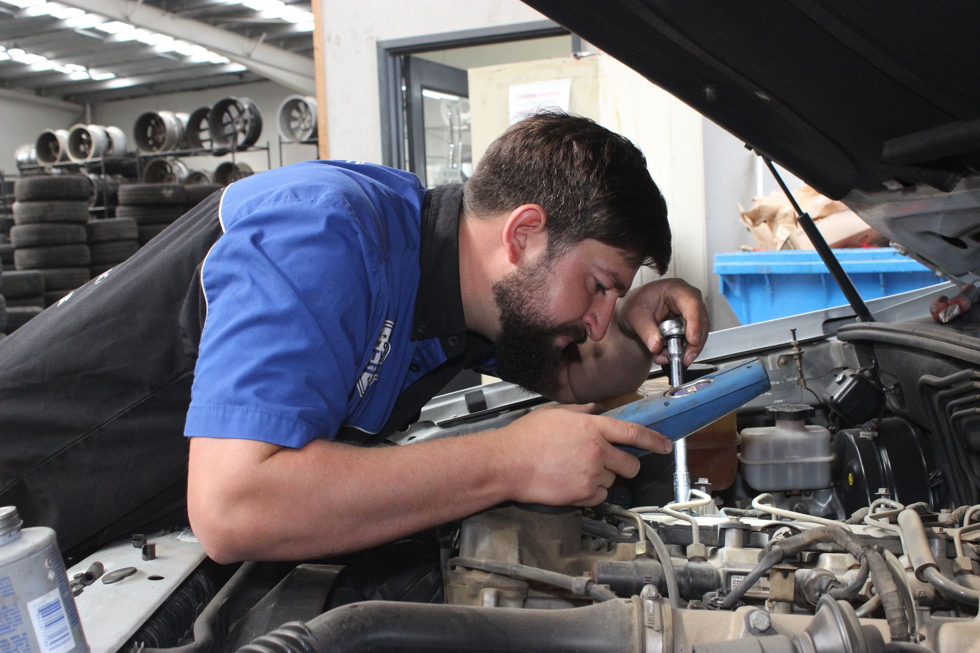 Mechanic in Blue Shirt Inspecting Car Engine Under Open Hood in A Garage — Bay City A1 Tyres in North Geelong, VIC