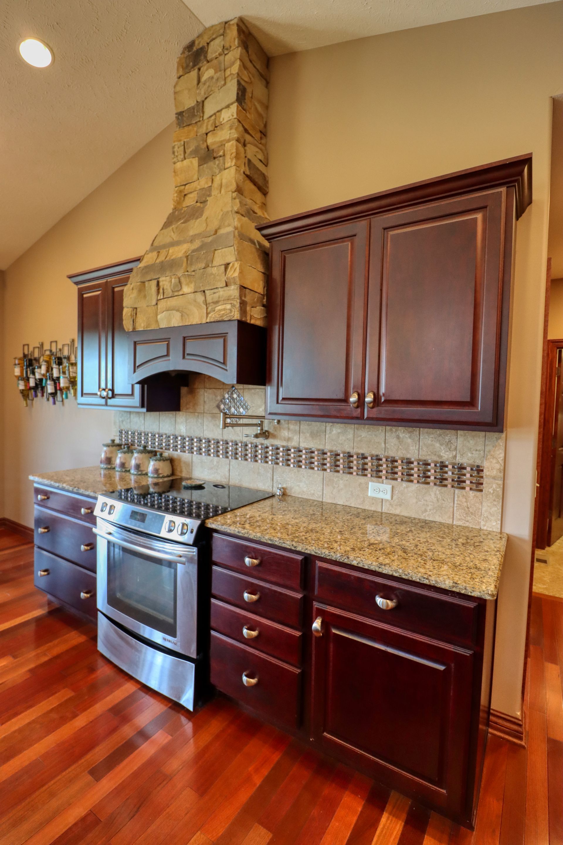A kitchen with wooden cabinets , stainless steel appliances , granite counter tops and a stone chimney.