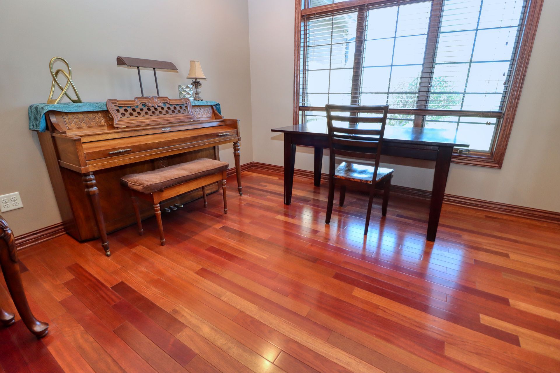 A room with hardwood floors , a piano , a desk and chairs.