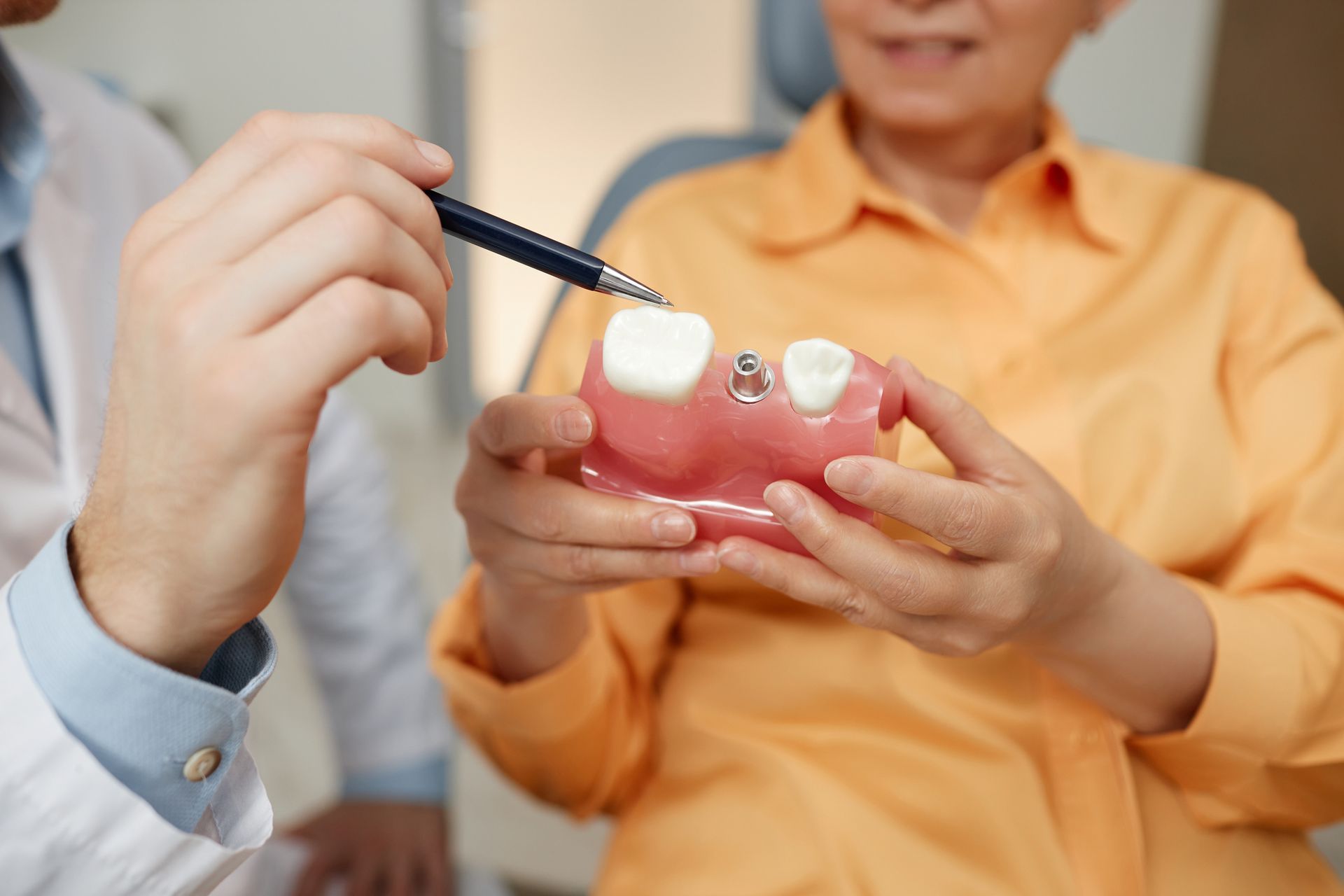 Dentist pointing at tooth model while explaining dental implant surgery