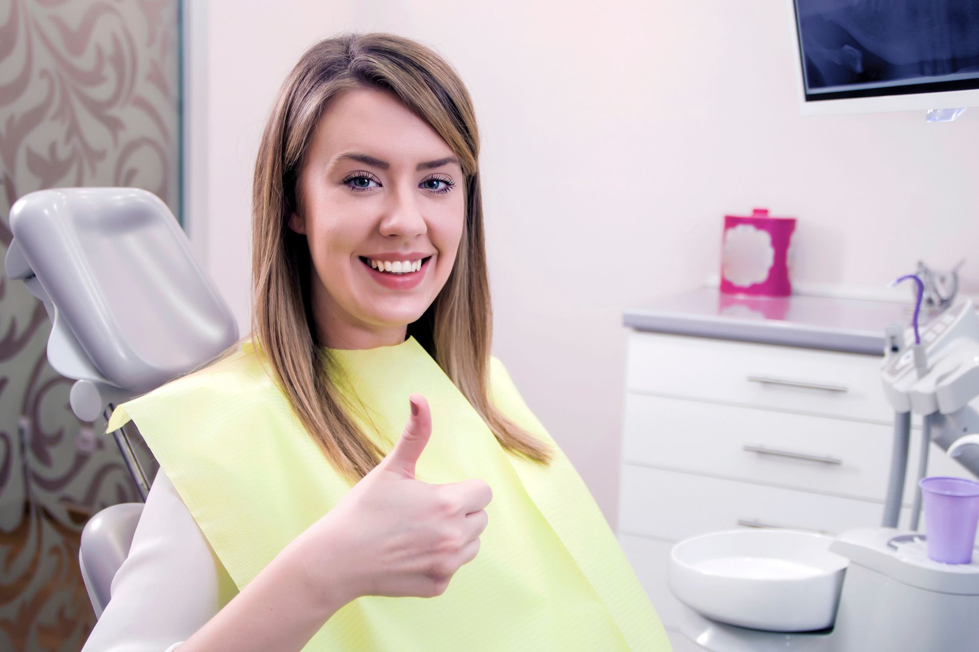 A woman is sitting in a dental chair and giving a thumbs up.