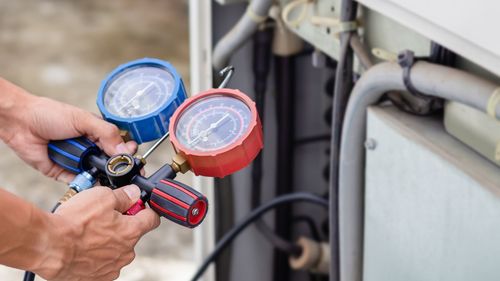 A person is holding two gauges in their hands while working on an air conditioner.