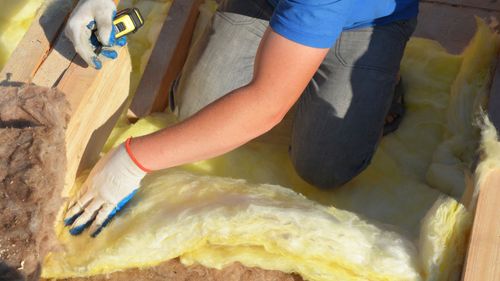 A person is kneeling down and measuring a piece of insulation.
