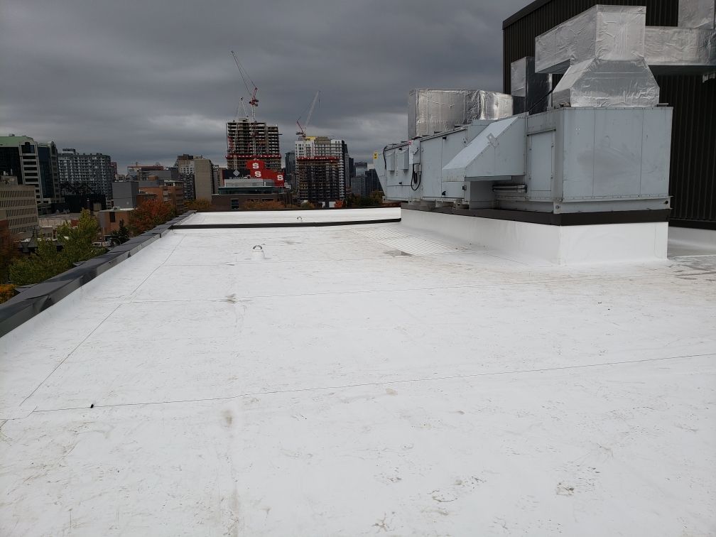 Toit plat blanc sur un bâtiment, paysage urbain en arrière-plan, ciel nuageux.