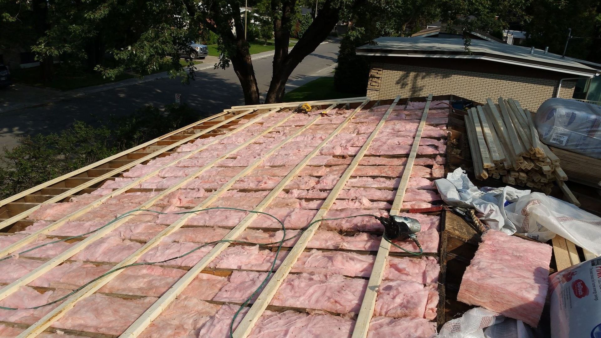 Un toit est en cours de construction avec une isolation rose et des poutres en bois.