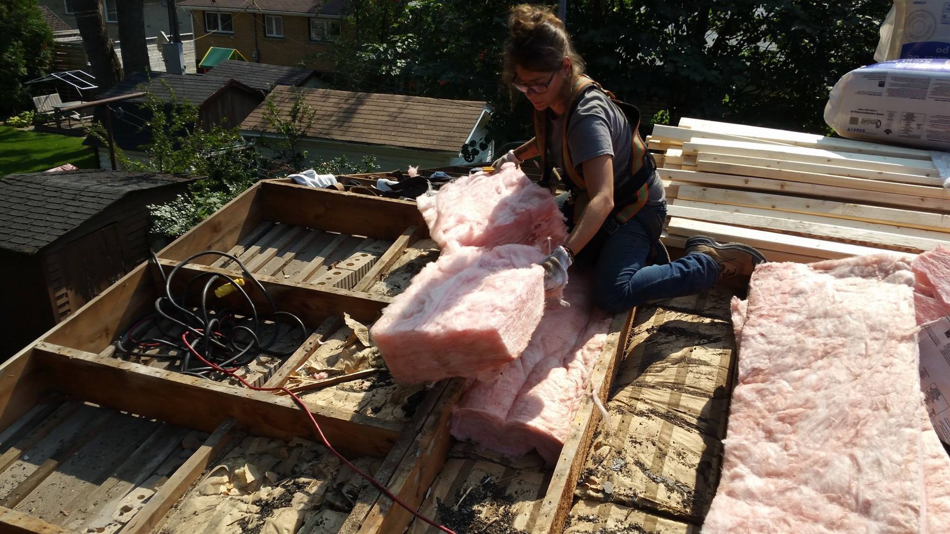 Une femme installe de l'isolant rose sur un toit. Lumière du soleil, extérieur.