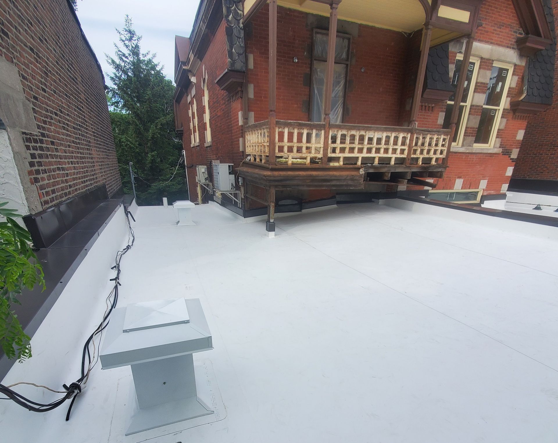 Toit blanc avec un système de ventilation, jouxtant un bâtiment en briques rouges doté d'un porche.