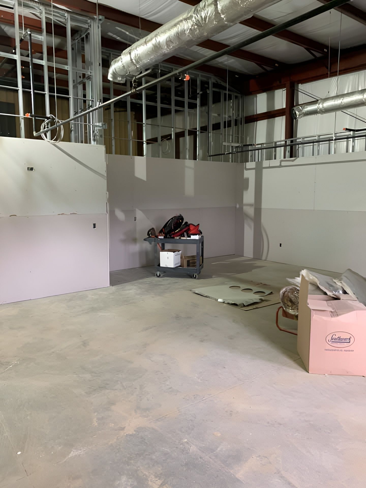 An interior view of a commercial space under construction with drywall partitions, exposed metal framing, and a utility cart.