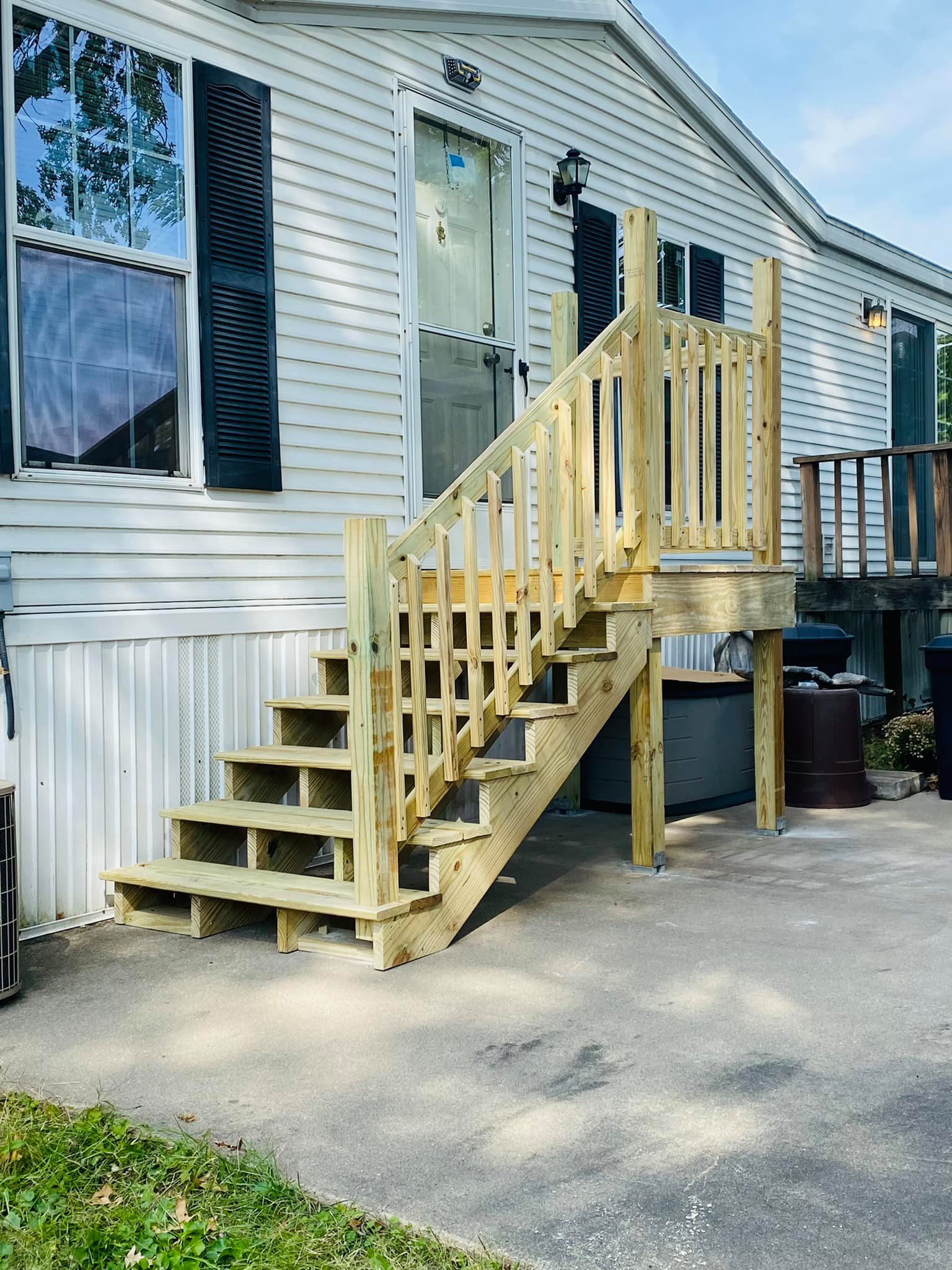 A newly built wooden staircase with railings leads up to the front entrance of a white mobile home.