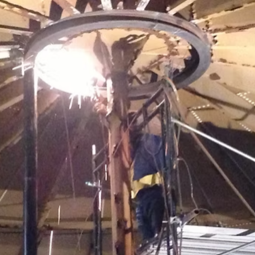 Man working on roof, adjusting a vent. Tools and paint can on the flat roof.