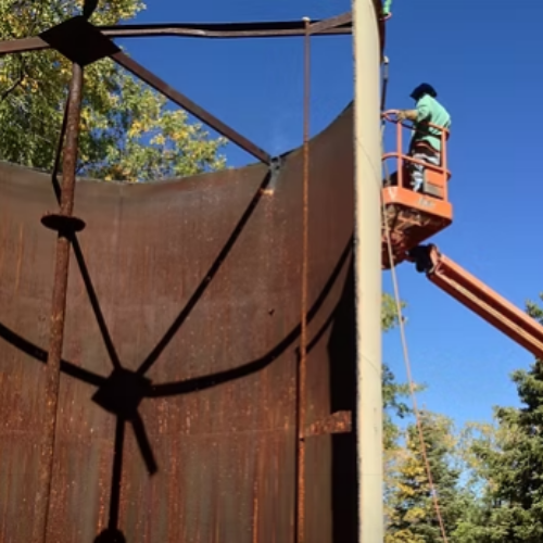 Man on roof repairs vent with tools and paint.