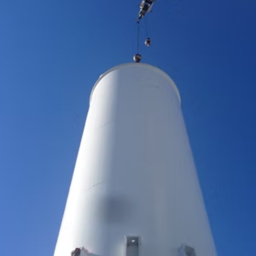 Black water tank atop rusty metal tower against a blue sky with clouds.