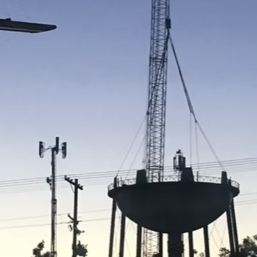 Black water tank atop a rusty metal tower against a blue sky with some clouds.