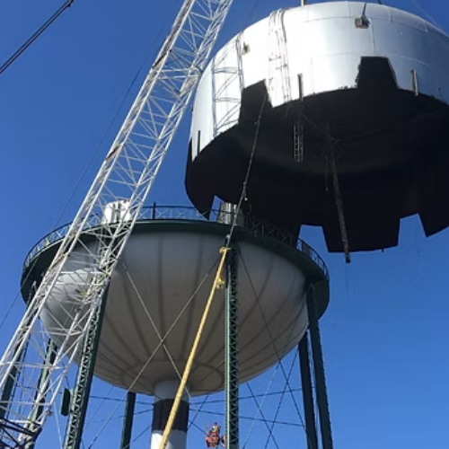 Black water tank atop rusty metal tower against a blue sky with clouds.