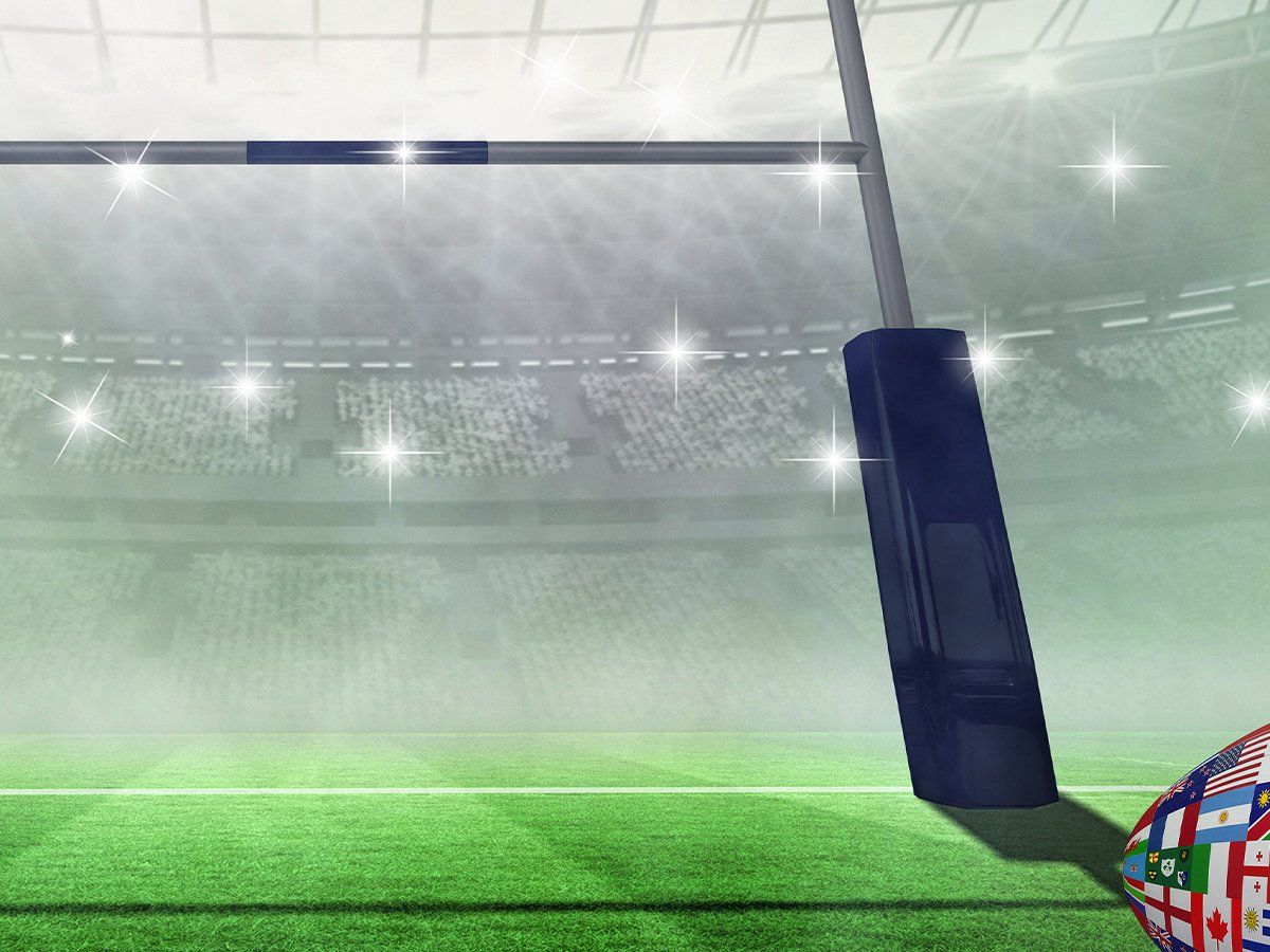 Rugby ball with world flags all over on field in lit up stadium.