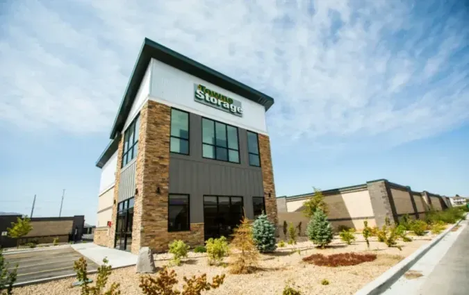 A modern two-story storage facility with stone facade and white upper siding under a bright blue sky.