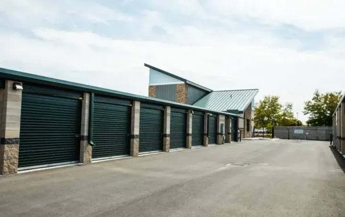 A row of dark green storage unit roll-up doors at an outdoor facility with a slanted, modern roof structure.