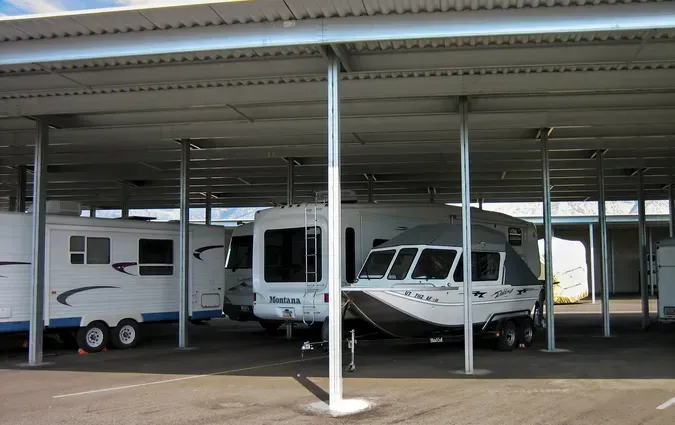 Several white recreational vehicles and a boat on a trailer parked under a large metal carport structure.