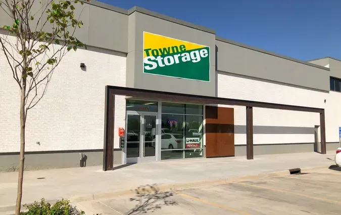 Exterior view of a Towne Storage facility entrance with a green and yellow sign above glass doors and a metal awning.