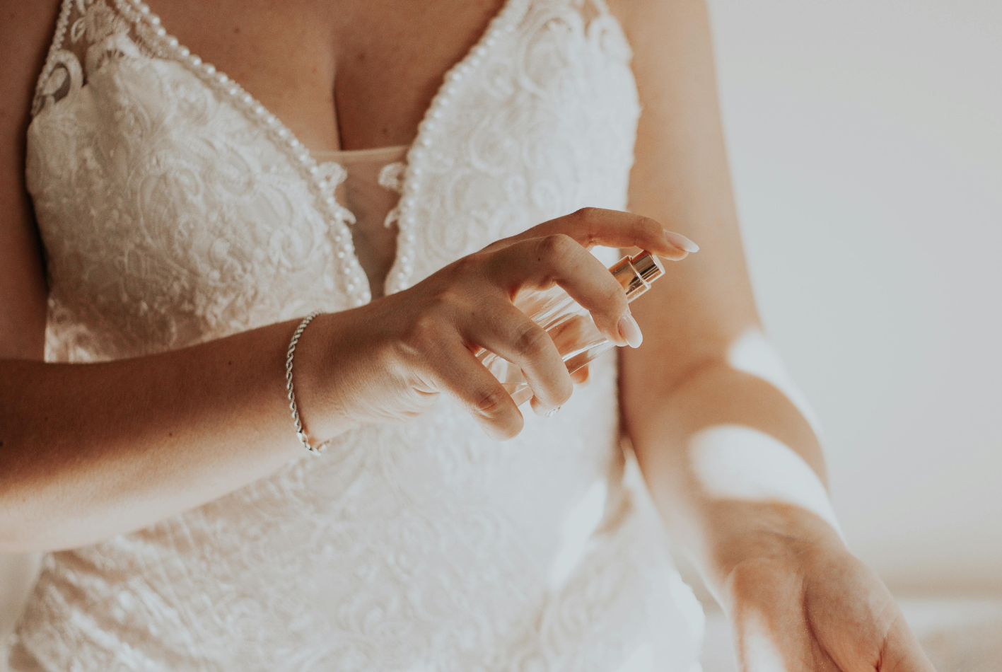 A woman in a wedding dress is spraying perfume on her hand.