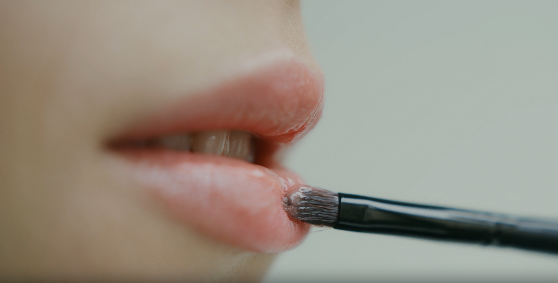A woman is applying lipstick to her lips with a brush.