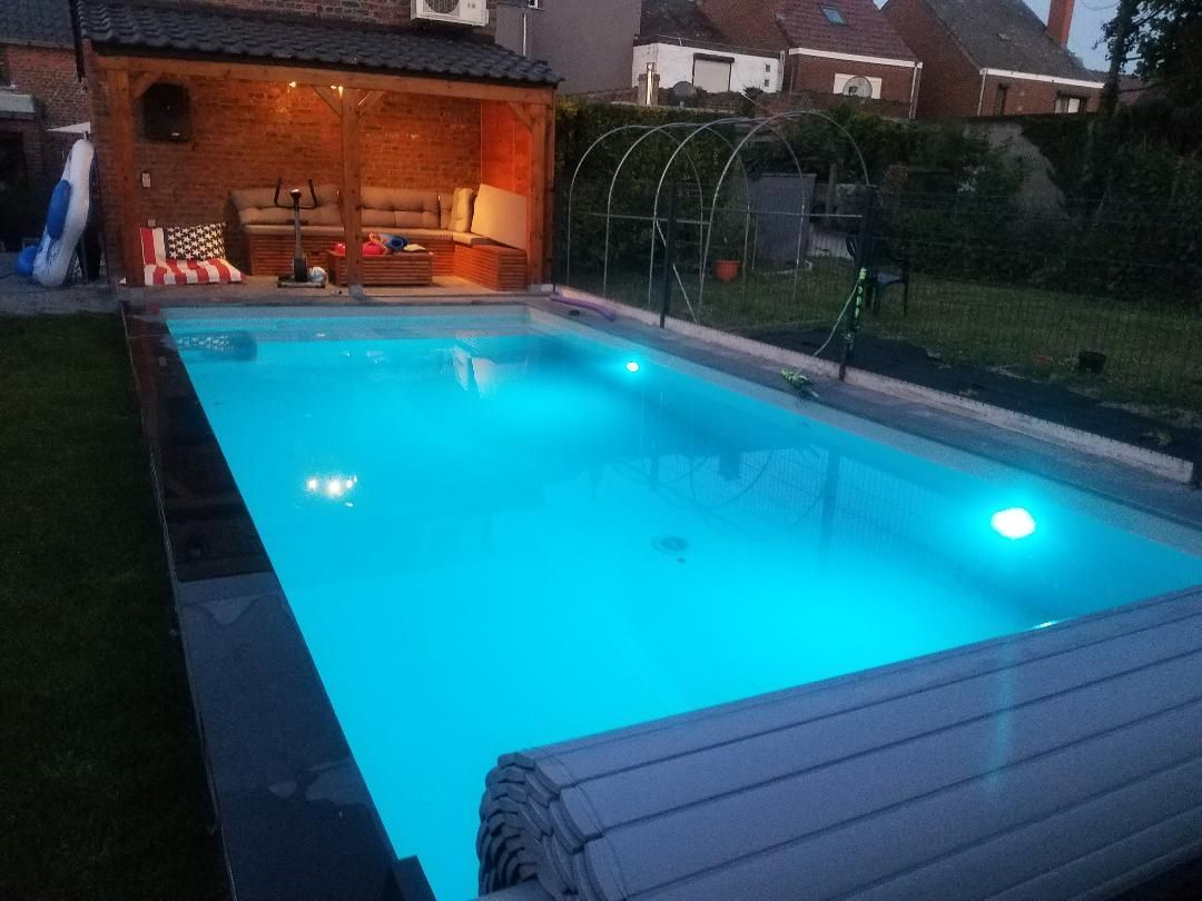 Une grande piscine est éclairée la nuit dans une cour arrière.
