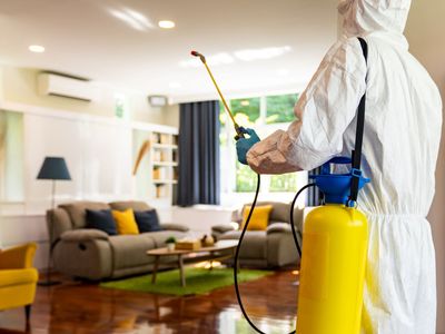 Un hombre con un traje de protección está rociando una sala de estar con un rociador.