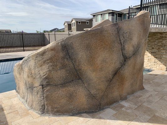 A large rock is sitting next to a swimming pool.