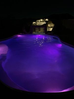 A swimming pool is lit up with purple lights at night.