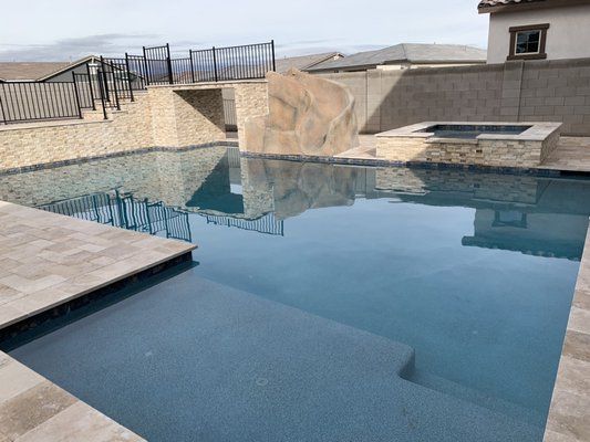 A large swimming pool with stairs and a hot tub in the backyard of a house.