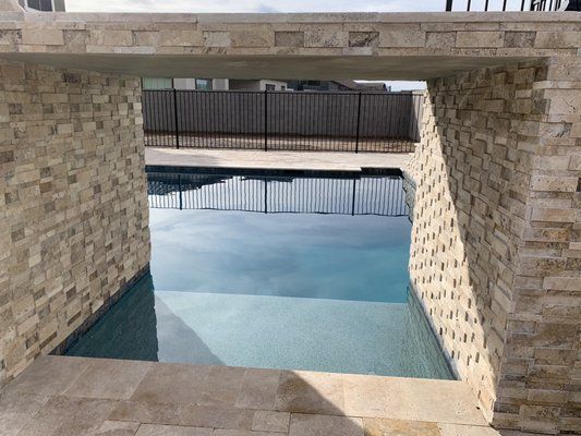 A swimming pool is surrounded by stone walls and a fence.