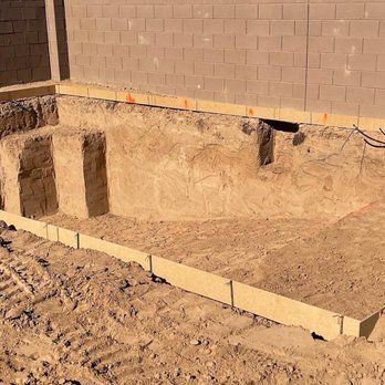 A swimming pool is being built in the dirt in front of a brick wall.