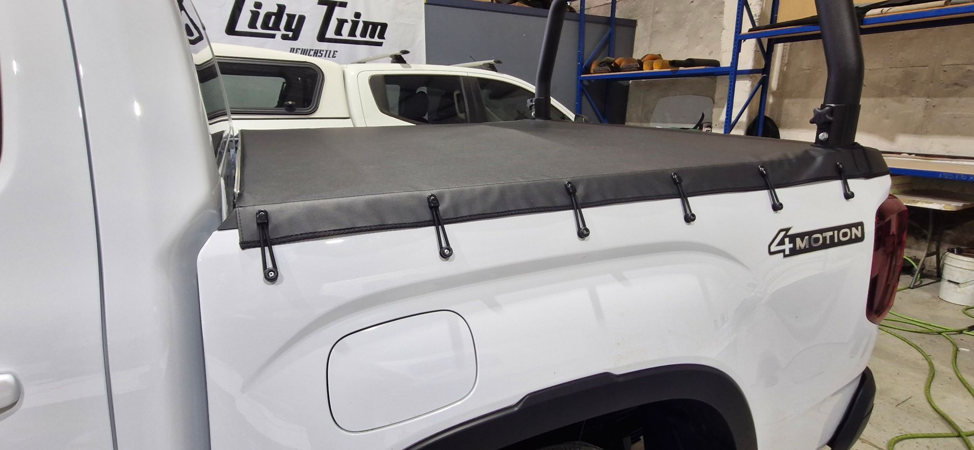 A white pickup truck with a black tonneau cover and roll bar in an industrial workshop — Tidy Trim Newcastle in Carrington, NSW