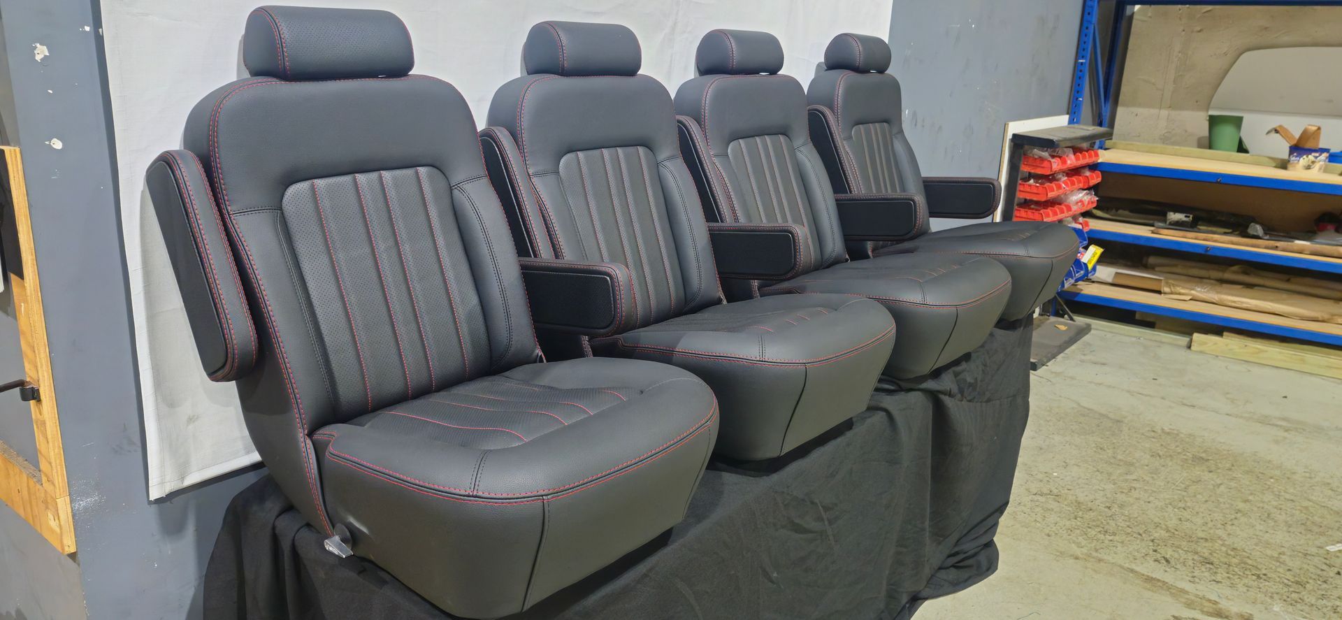 Four black bucket seats with red stitching are lined up on a black base inside a workshop — Tidy Trim Newcastle in Carrington, NSW