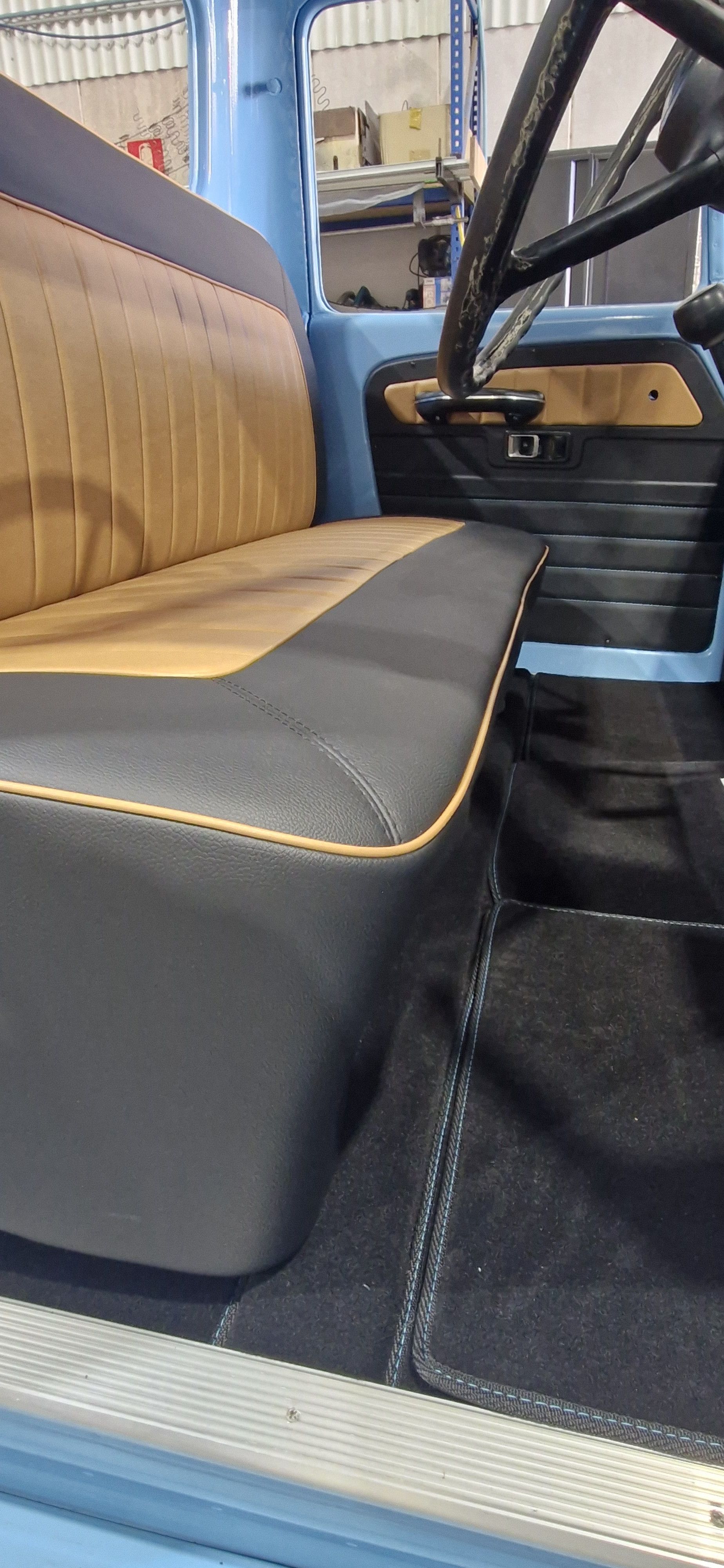 A vehicle interior showing a bench seat upholstered in tan and dark gray leather, matching door panels, and dark carpeting — Tidy Trim Newcastle in Carrington, NSW