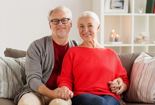 An elderly couple is sitting on a couch holding hands.